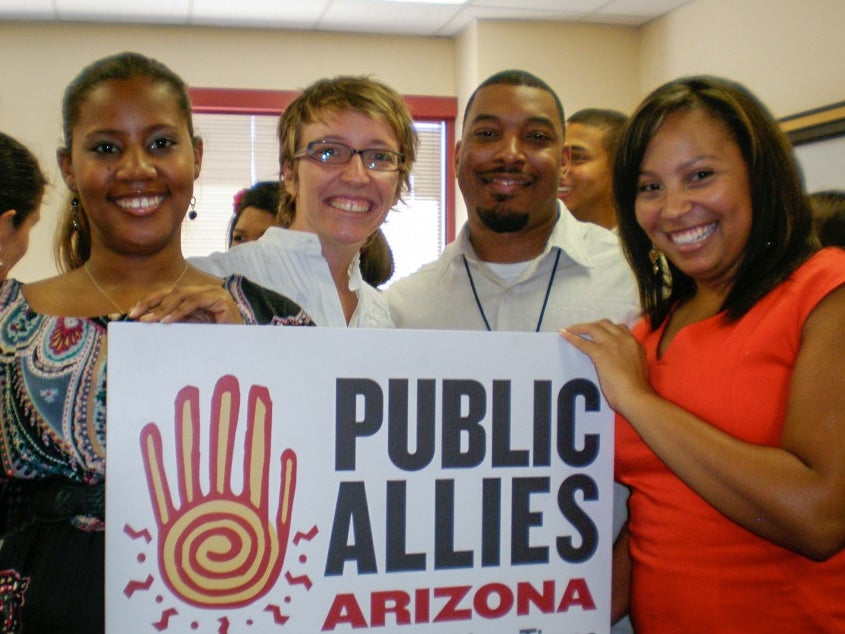 Four people pose around a small sign for Public Allies Arizona.