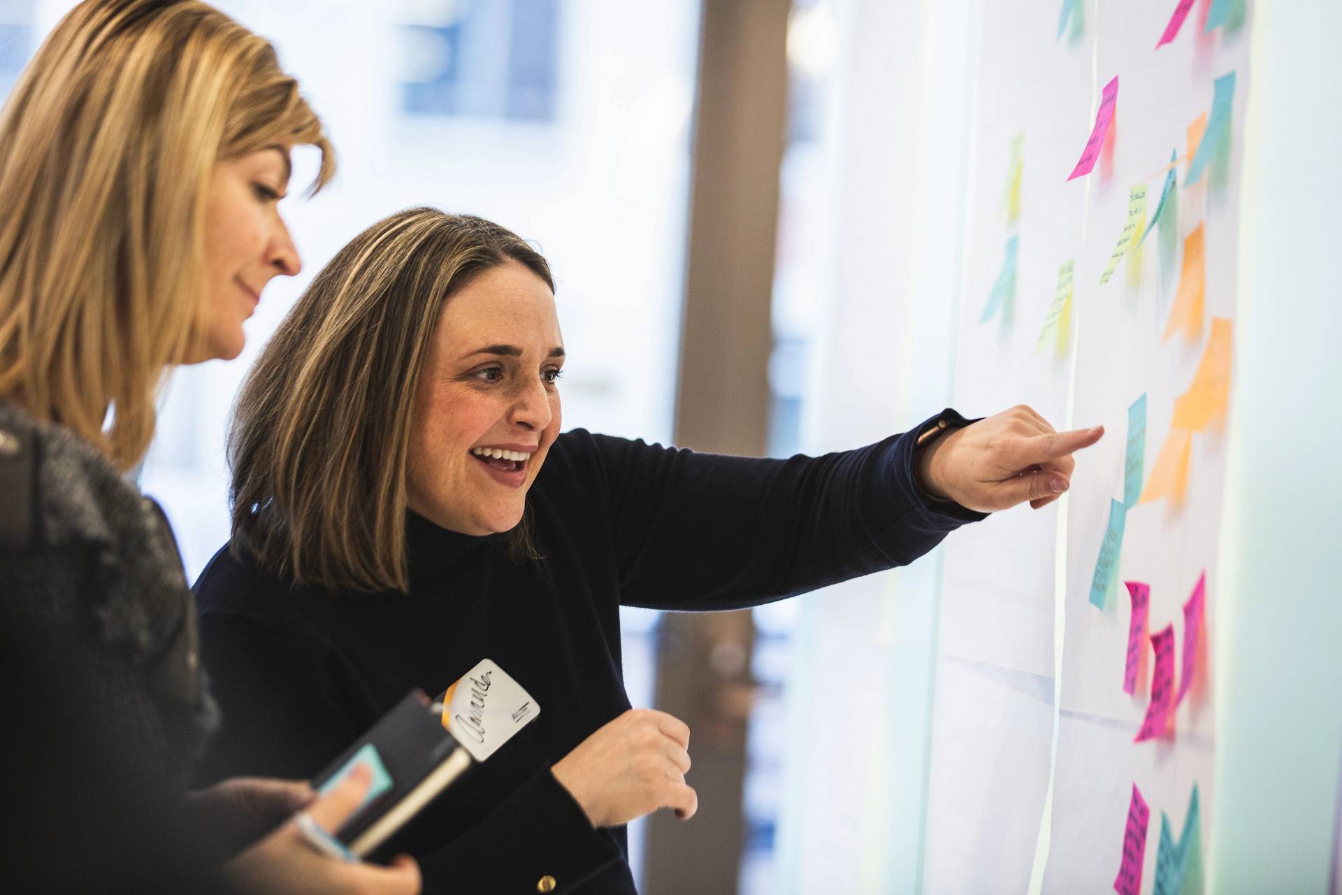 Two women add sticky notes to a whiteboard