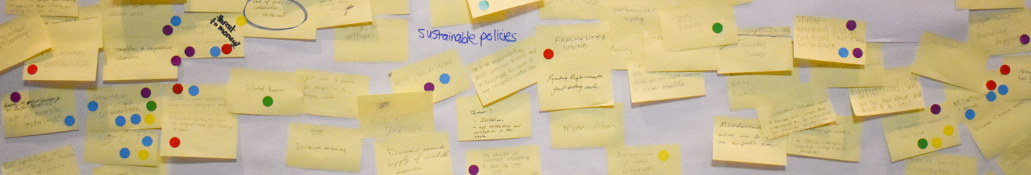 A large white paper is almost completely covered with yellow post-it notes with writing. The words "sustainable policies" are written on the white paper background. There are colored circles added to the image for visual effect.