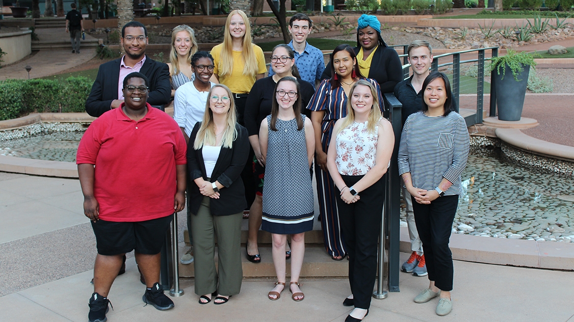 Members of the Nonprofit Leadership Alliance Student Association smile while outside. Behind them is a small artifical river with a bridge crossing over it.