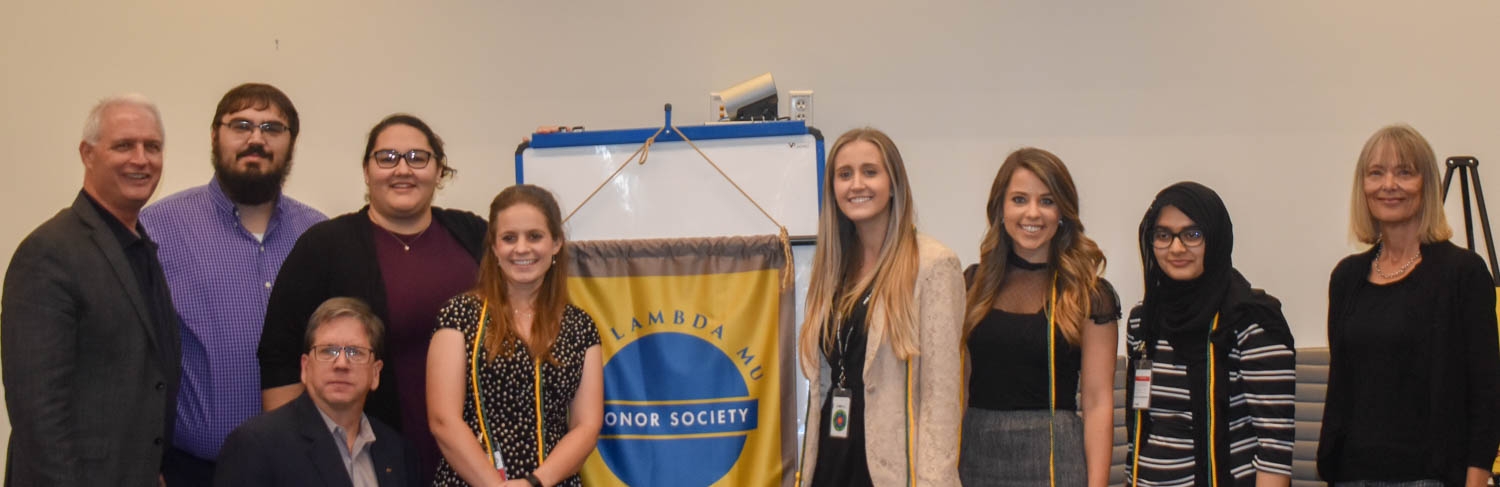 Fall 2019 inductees of the Nu Lambda Mu Honor Society from Arizona State University stand next to a banner for the society.