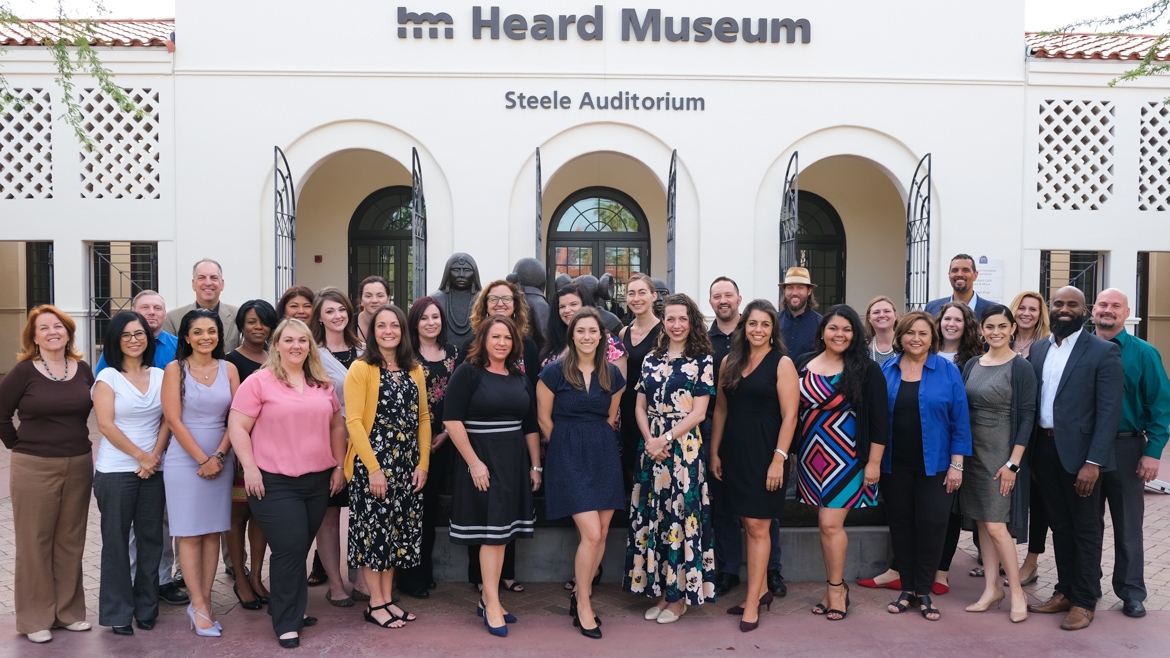 A large group of smiling people stand in front of the Heard Museum in Phoenix, Ariz., in spring 2019.