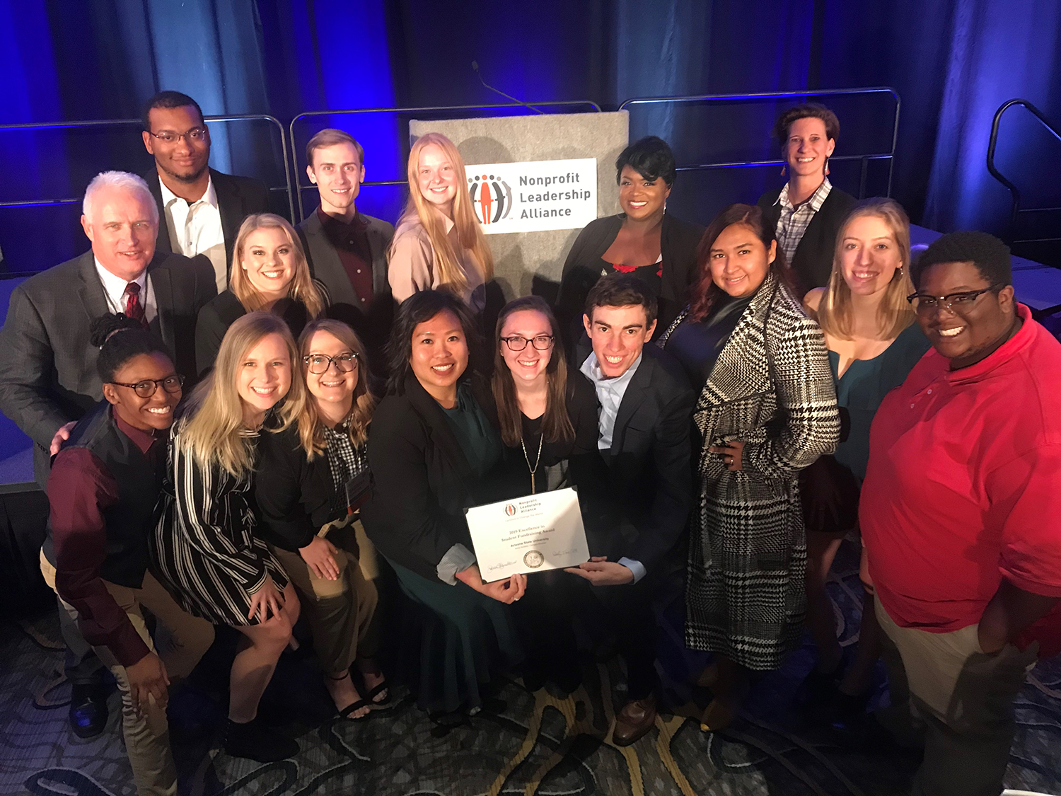 Inside a conference room, Nonprofit Leadership Alliance Student Association members pose with a paper cerificate for Excellence in Student Fundraising Award.