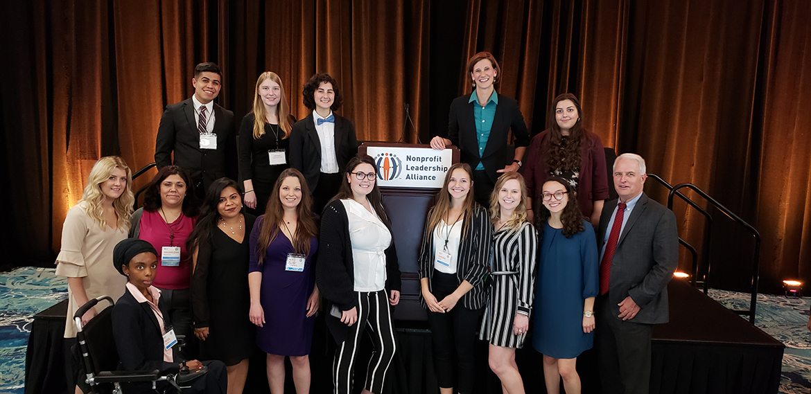Standing in front of a stage with a podium and "Nonprofit Leadership Alliance" sign, students pursuing the Certified Nonprofit Professional Credential stand alongside ASU faculty. 