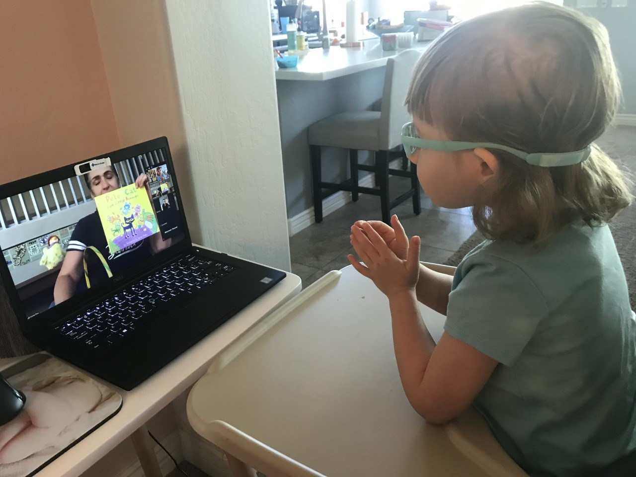 A kid with elastic-band glasses sits and watches a video on a laptop.