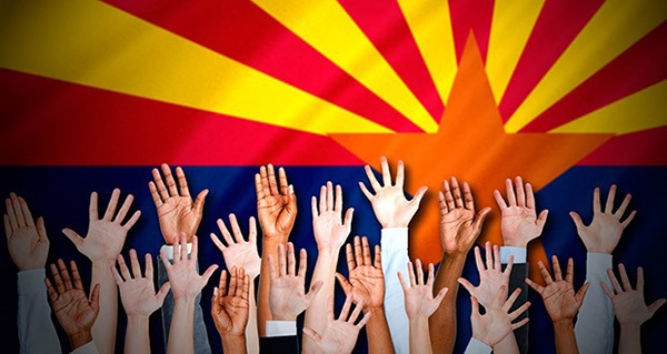 Several hands are raised in front of an Arizonan flag.