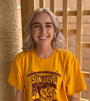 Haylee Davis outside and in front of a building pillar. They are wearing an shirt with ASU maroon and gold colors.