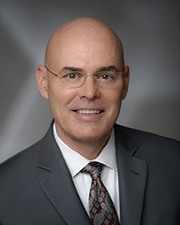 A professional photo of John Phelps smiling while wearing a suit.