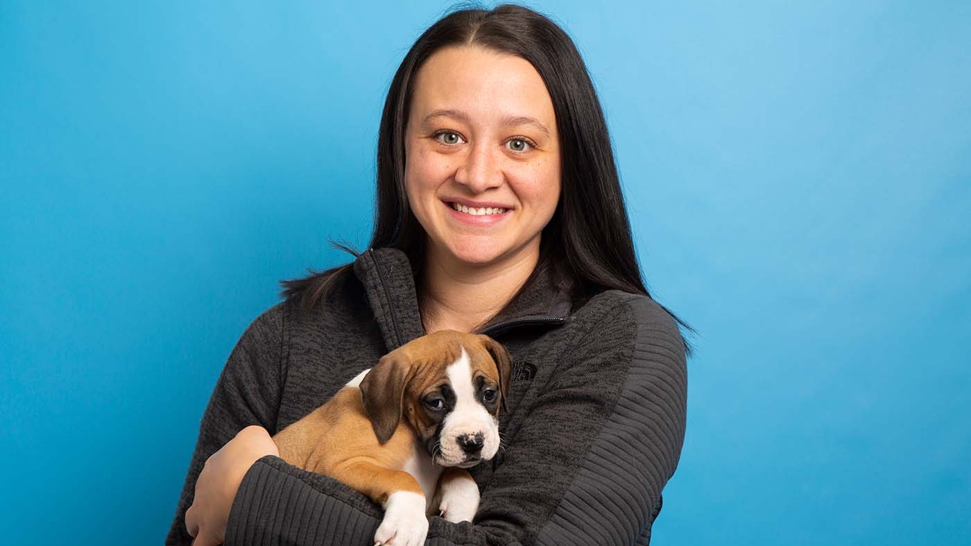 Kayla Weber smiles while holding a puppy in front of a blue background.