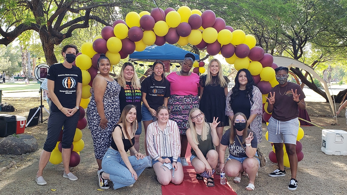 Nonprofit Leadership Alliance Student Association students and supporters gather in front of an archway maroon and gold balloons in a park.