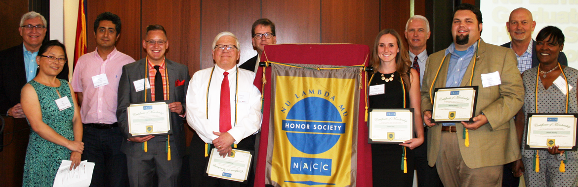 Nu Lambda Mu Nonprofit Honor Society members stand next to a Nu Lambda Mu Nonprofit Honor Society banner. Some are holding framed certificates.