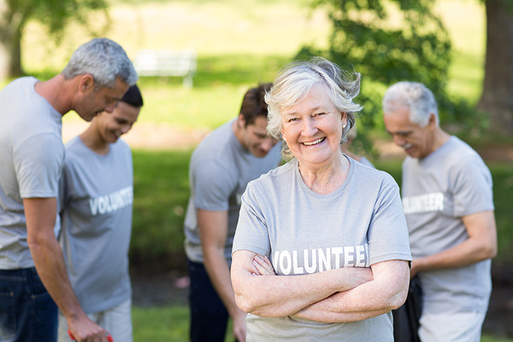 Several senior volunteers are in an outside park. One volunteer crosses their arms and smiles at the camera.