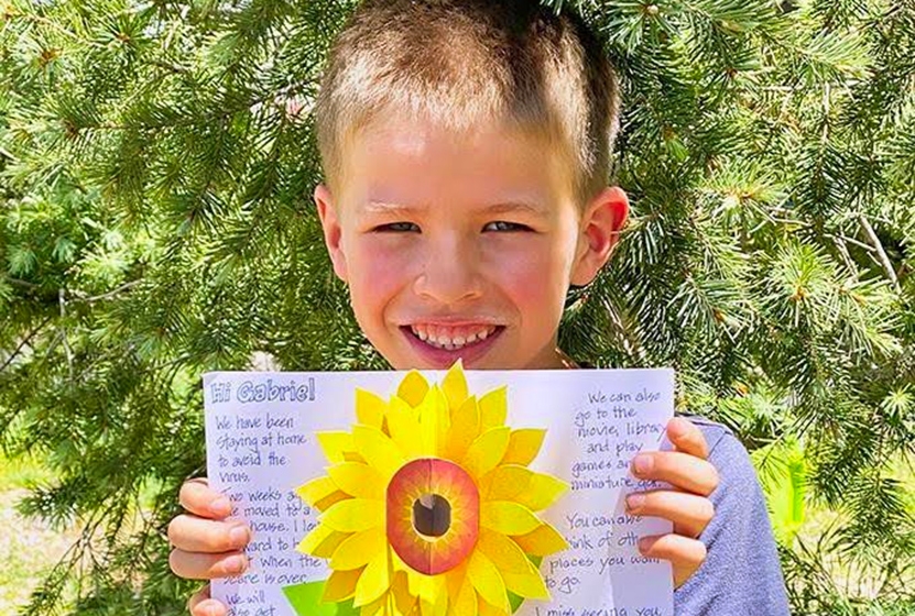 A kid named Gabriel holds up a hand-written card from their Big Brother. The card has a pop-up sunflower in the center.