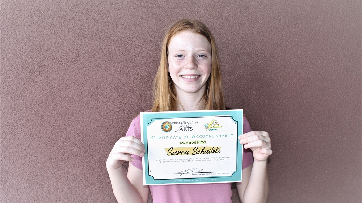 A young person smiles while holding up a paper certificate.